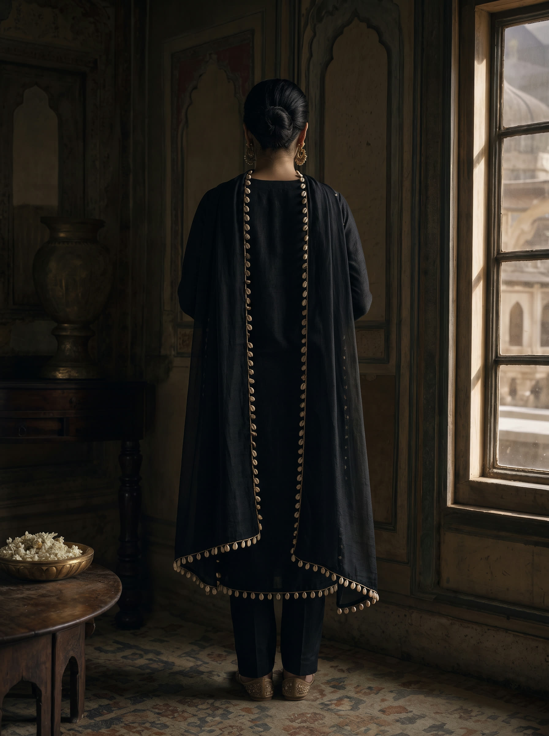 Kaudi back view — A kohl-black silk suit edged with real cowrie shells — the old protective charm, worn quietly.