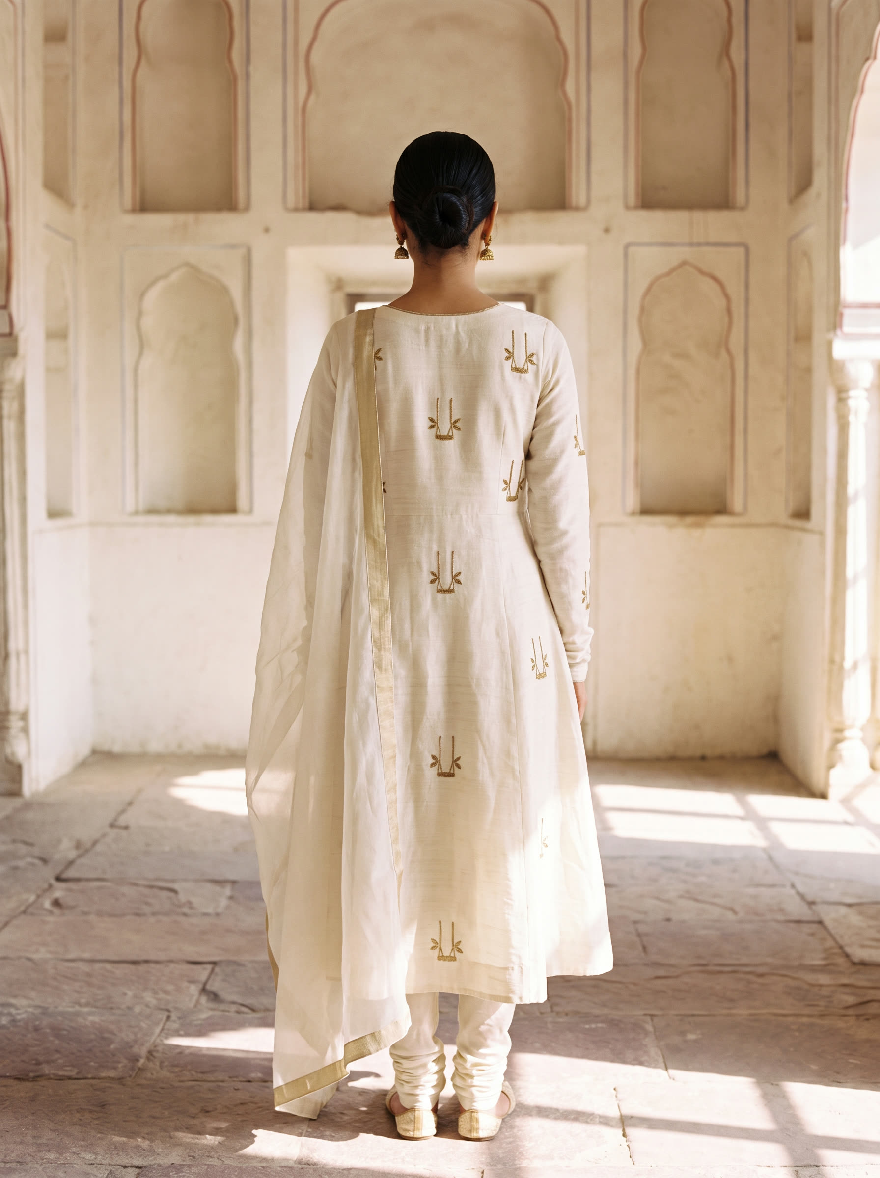 Peengh back view — The house signature. Ivory silk anarkali with scattered peengh motifs hand-worked across the kurta and sleeves in antique matte gold — the emblem of the house, repeated softly.